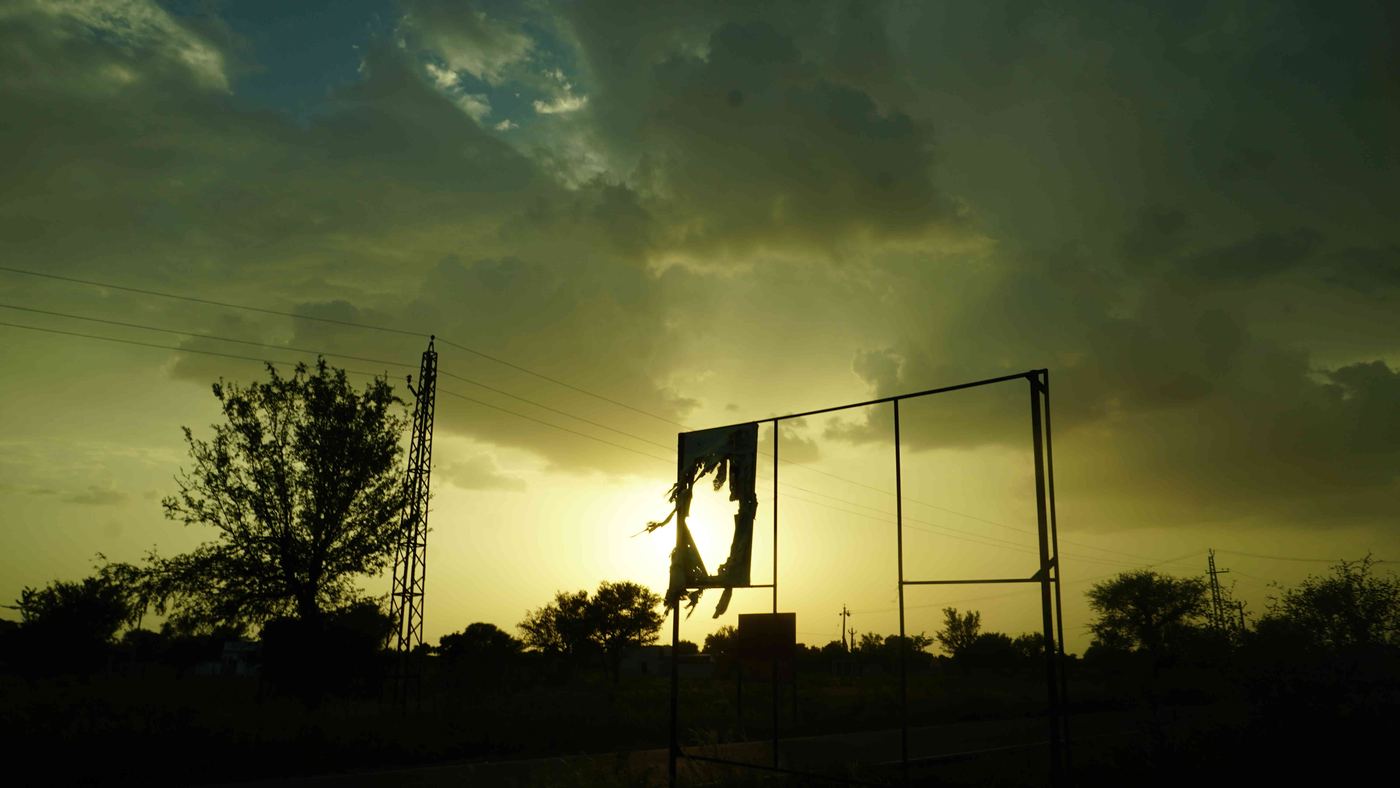 A torn advertising hoarding against a monsoon dusk sky